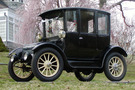 The 1916 Rauch & Lang Electric Brougham, it's an all black car with white wheel spokes in front of a blooming cherry tree