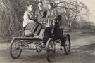 A black and white photo of three people riding on the 1901 Stanley Mobile, Lex, Irene & Barbra DuPont, two men and a woman 