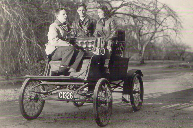 A black & white photo of three people sitting in the 1901 Stanley Mobile, which looks more like a carriage than a car