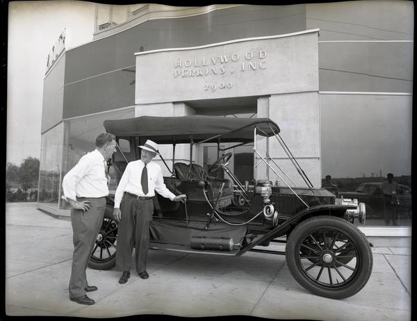 James F. Hollywood and T. Clarence Marshall stand in front of a 1910 Stanley Model 71 at Hollywood-Perkins Desota & Plymouth Dealership, the photo is fully black and white